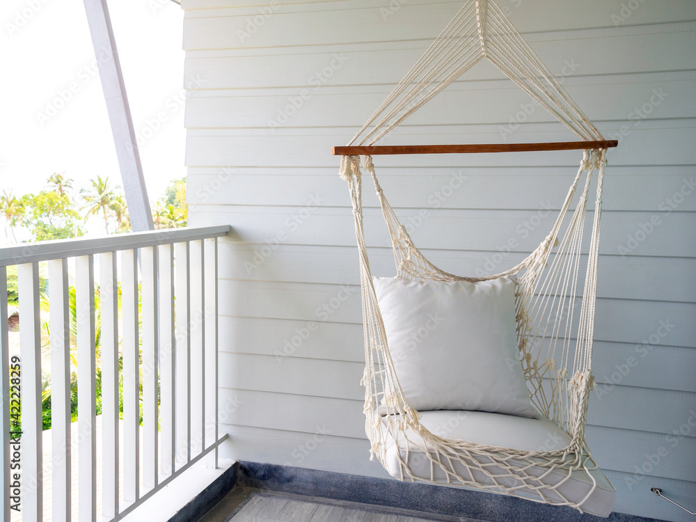 Empty white knitting rope swing hanging from ceiling on white wood  background in room terrace in the resort. Vintage white handcraft hammock  decoration on balcony. Stock Photo