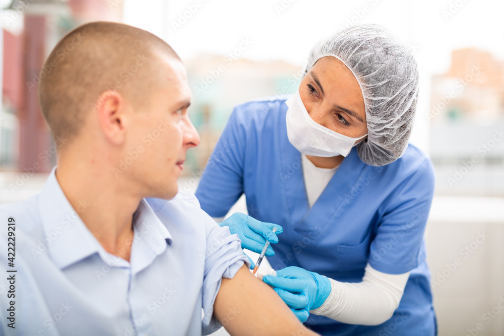Doctor in a protective mask injects a vaccine to a man with a syringe