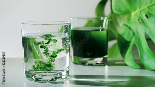 Chlorophyll extract is poured in pure water in glass against a white grey background with green leaf. Liquid chlorophyll in a glass of water. Concept of superfood, healthy eating, detox and diet photo