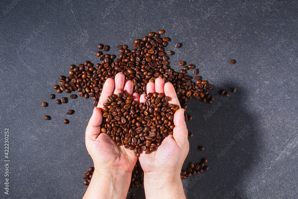 Roasted brown coffee beans on a gray background. Template for advertising coffee in shape heart in hand. Top view. Roasted brown coffee beans on a gray background. Template for advertising coffee in shape heart in hand. Top view.