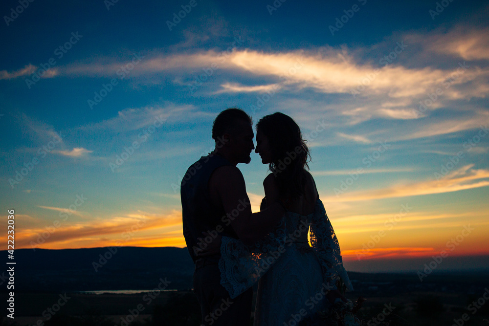 Silhouette of a couple hugging and kissing at sunset against the background of mountains and sea.