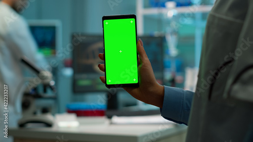 Chroma key isolated display on smartphone used by scientist woman in lab cabinet and colleagues in white coat bringing blood sample. Scientist using mobile phone with mockup green screen