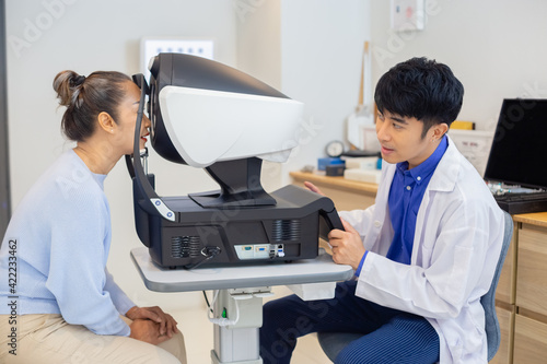 Ophthalmologist examining eyesight modern machine for middle aged asian woman. Checking eye vision by optician health examination concept.