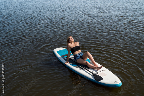 Young female surfer lying on sup board and rest at nature