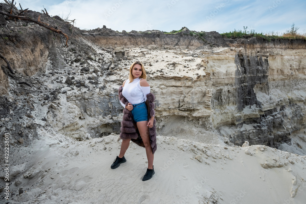 portrait of astonishing young woman wearing fur coat in dry empty sand quarry