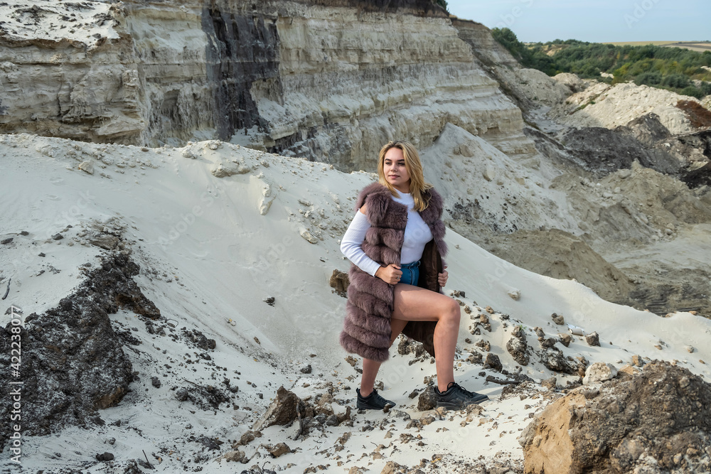portrait of young lady with fur coat and casual cloth posing near sand rocks