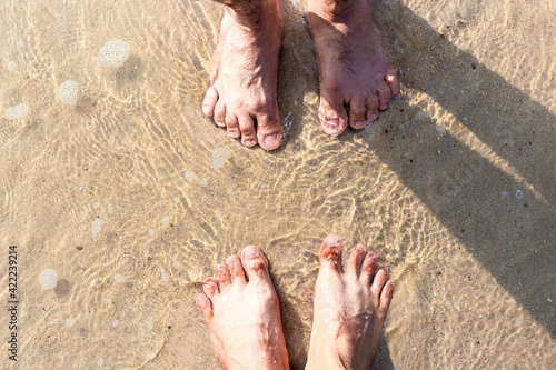 Feet of two men stepping on the sand in the sea.