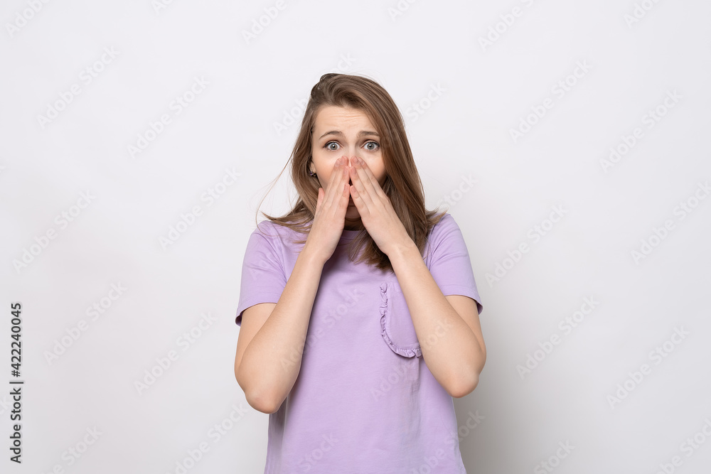 Shocked young woman covering her mouth with hands, isolated on gray background Shocked young woman covering her mouth with hands, isolated on gray background