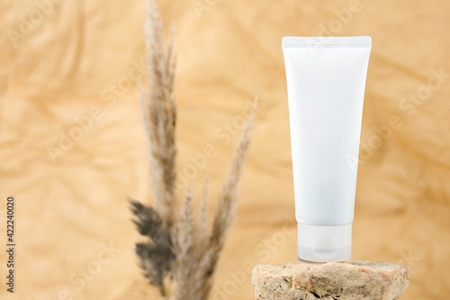 White squeeze bottle plastic tube for branding of medicine or cosmetics - cream, gel, skin care. Cosmetic bottle container on rock on beige brown blurred background, cosmetic packaging mockup.