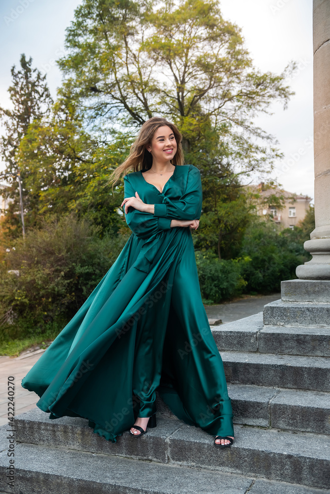 Naklejka premium full length young elegant woman in beautiful green gress standing in stone stair