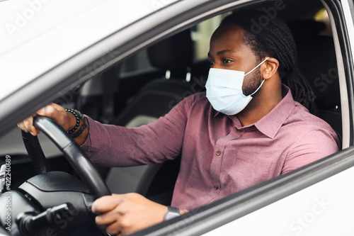 African American male taxi car driver wearing protective face mask or respirator for protection against viral diseases, sitting at the front, behind the wheel. Healthcare, safety in pandemic concept © Vadim Pastuh