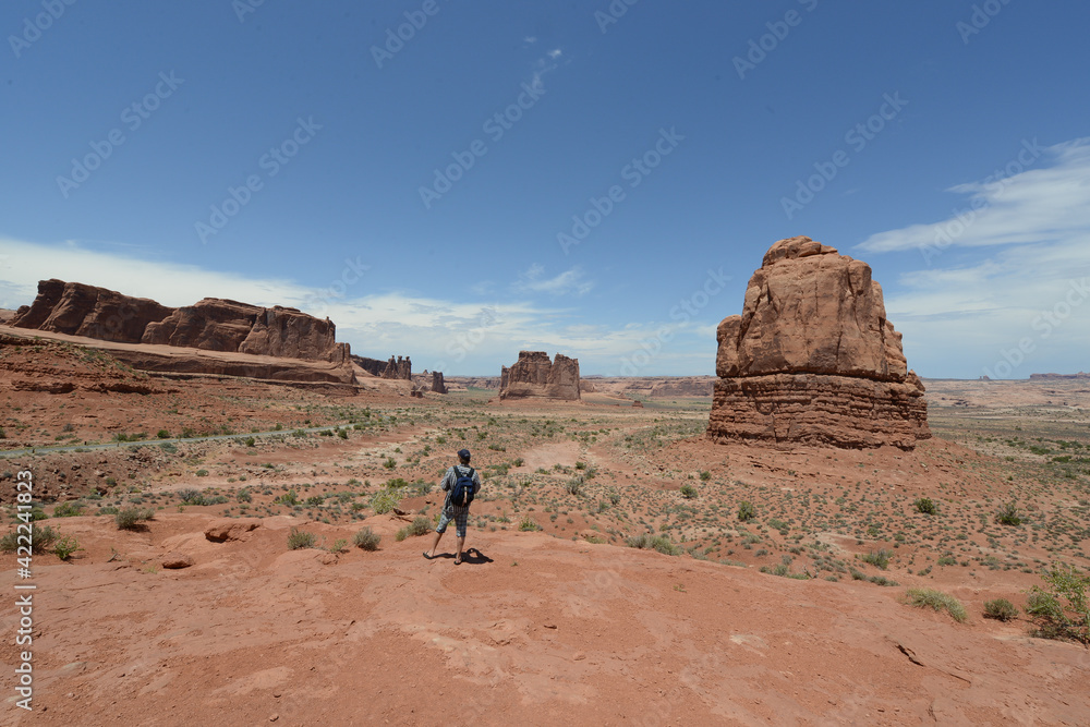 A hiker looking at the vast landscape and red sandstone formations at Arches National Park in Utah on a sunny day