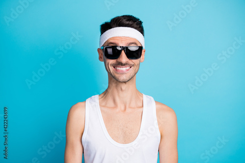 Portrait of good mood sportive guy in sunglass look camera isolated over blue color background © deagreez
