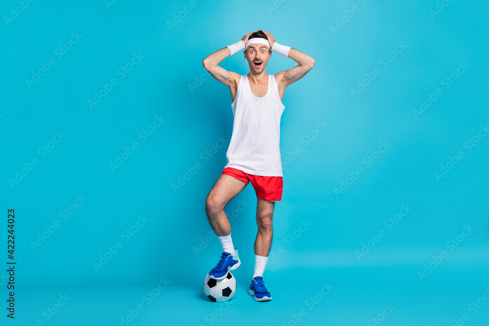 Full body portrait of impressed young man arms on head open mouth leg on ball isolated on blue color background