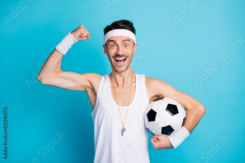 Photo of excited soccer player hold ball raise fists muscles wear white tank-top isolated over blue color background © deagreez