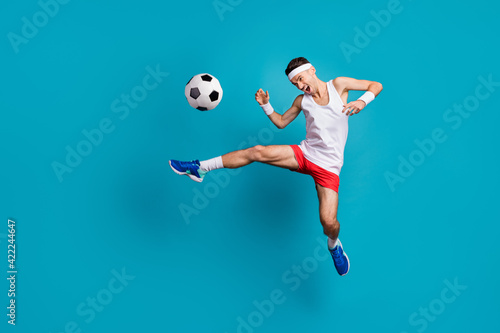 Fototapeta Naklejka Na Ścianę i Meble -  Full length photo of crazy football player kick ball in jump wear white tank-top isolated over blue color background