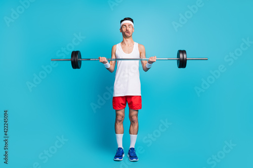 Photo of young sportsman lift heavy barbell grimacing exercise bodycare isolated over blue color background