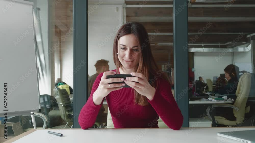 Young attractive woman hipster playing mobile game and lose. Caucasian woman focus on beating his opponent and lose while playing his game, very upset with office background. Young attractive woman hipster playing mobile game and lose. Caucasian woman focus on beating his opponent and lose while playing his game, very upset with office background.