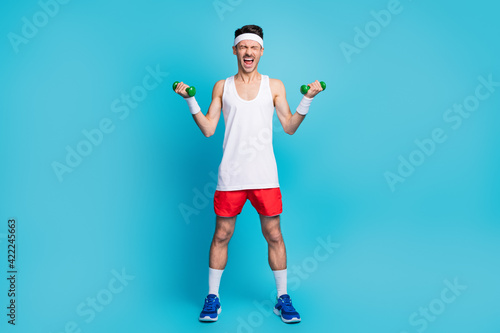 Fototapeta Naklejka Na Ścianę i Meble -  Full size photo of young sportsman do exercise scream heavy dumbells workout isolated over blue color background
