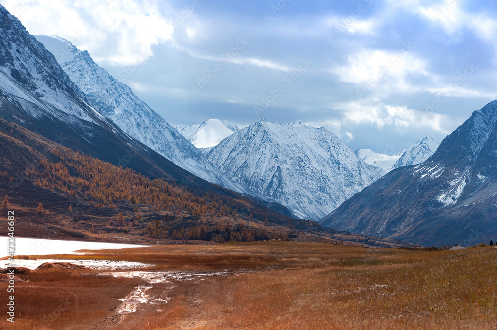Scenic view over Akkol valley, surrounded by snow capped mountain range, dramatic sky and clouds. Altai autumn landscape, Russia