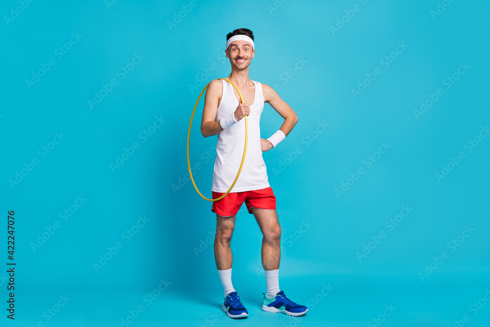 Full size portrait of cheerful man out hand on waist hold hula hoop beaming smile isolated on blue color background