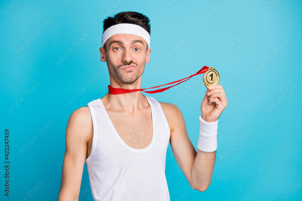 Photo of young sportsman serious hold gold medal win victory competition isolated over blue color background Photo of young sportsman serious hold gold medal win victory competition isolated over blue color background