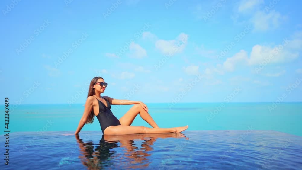 Young Woman in Black Swimming Suit Sitting on the Edge of Infinity Pool on Turquoise Seascape Background Wearing Sunglasses on a Sunny Day Slow Motion
Young Woman in Black Swimming Suit Sitting on the Edge of Infinity Pool on Turquoise Seascape Background Wearing Sunglasses on a Sunny Day Slow Motion