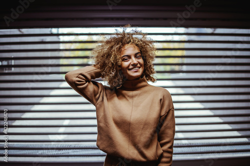 Smiling mixed race rap girl standing in front of garage door and looking at camera.