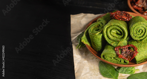 Vegeterian green pancakes decoraten with dried tomato. Spinach pancakes in a brown plate on dark background. Copy space. photo