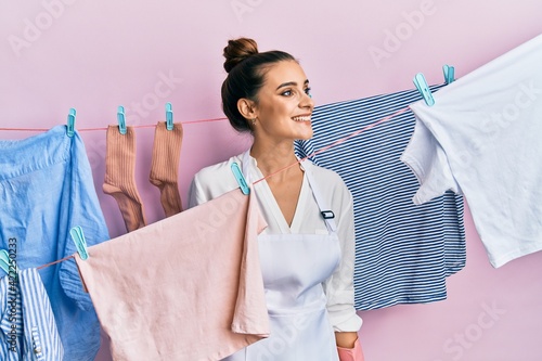 Beautiful brunette young woman washing clothes at clothesline looking away to side with smile on face, natural expression. laughing confident.