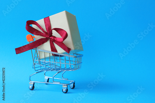 Box with ribbon in a shopping cart on a blue background with space for text. Purchase a gift. photo