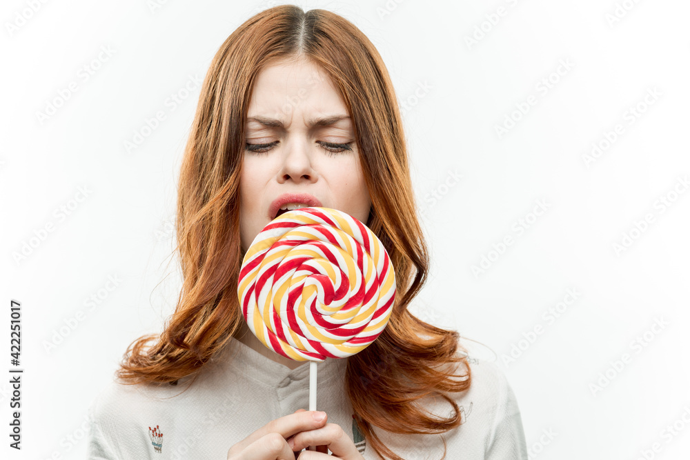 cheerful red-haired woman with a big lollipop in her hands emotions sweets lifestyle light background