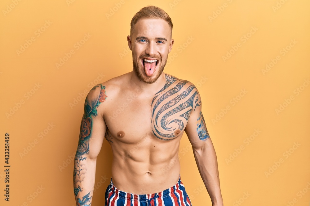 Young caucasian man wearing swimwear shirtless sticking tongue out happy with funny expression. emotion concept.