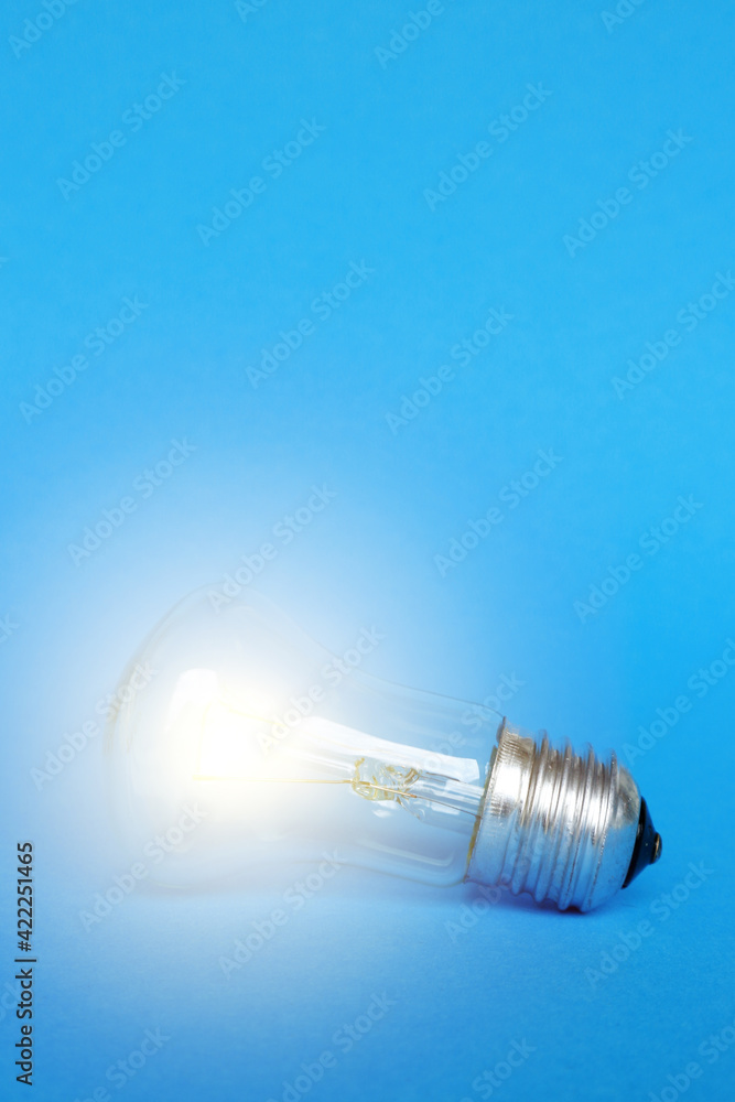 A glowing light bulb on a blue background. Vertical photo. A glowing light bulb on a blue background. Vertical photo.
