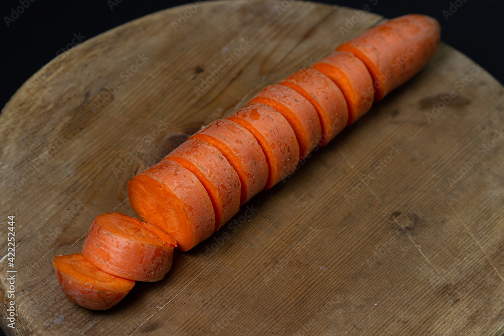 Carrots on a dark background. Sliced carrots on a wooden board on a black background. Healthy food