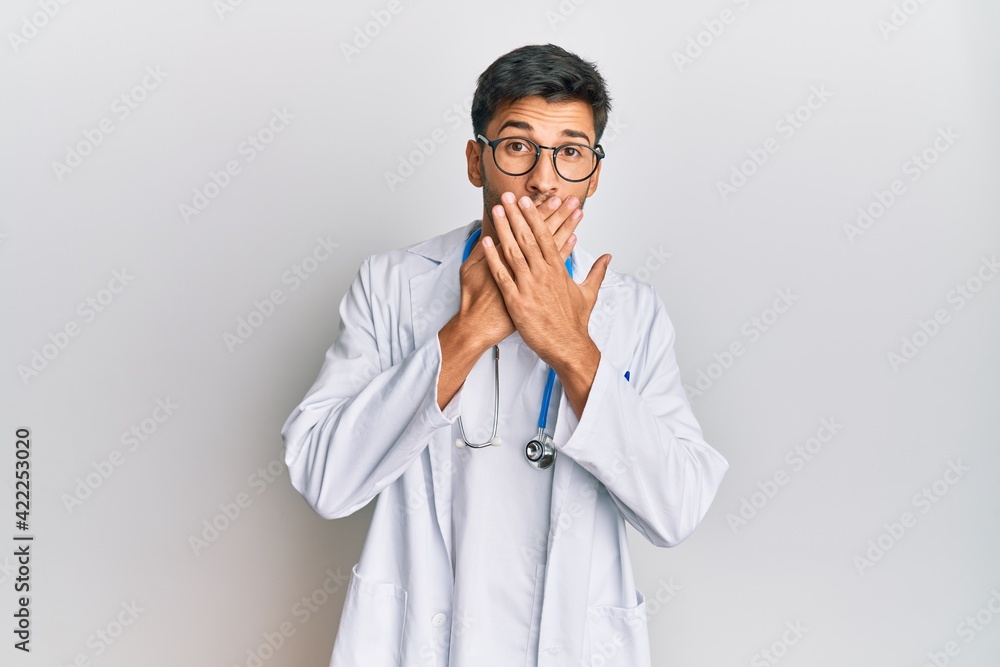 Young handsome man wearing doctor uniform and stethoscope shocked covering mouth with hands for mistake. secret concept. Young handsome man wearing doctor uniform and stethoscope shocked covering mouth with hands for mistake. secret concept.