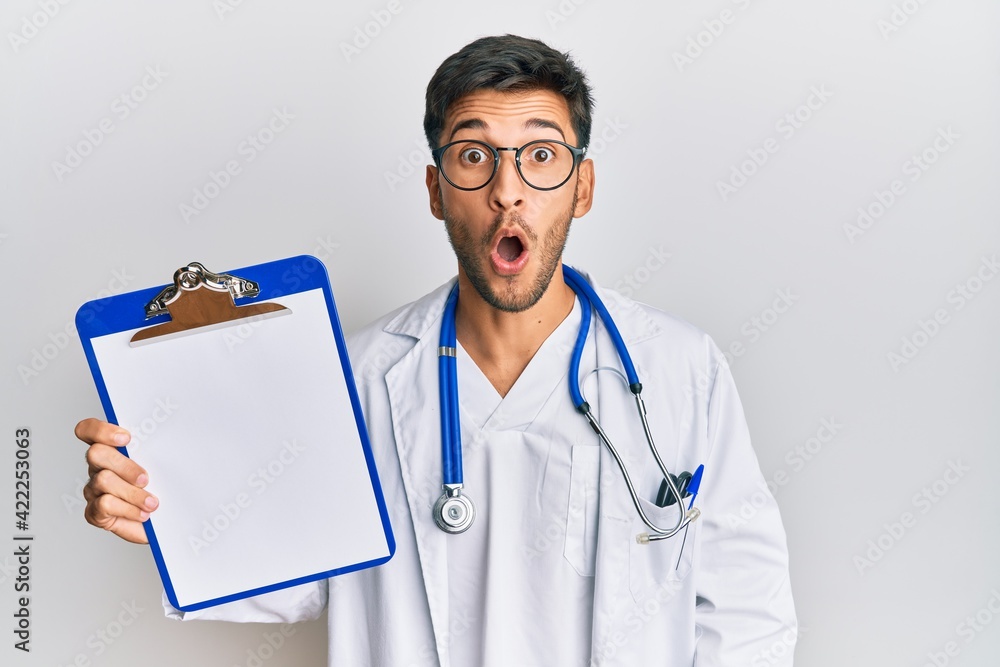 Young handsome man wearing doctor stethoscope holding clipboard scared and amazed with open mouth for surprise, disbelief face Young handsome man wearing doctor stethoscope holding clipboard scared and amazed with open mouth for surprise, disbelief face