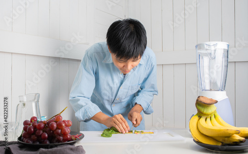 Enjoying Asian man slicing vegetables preparing to Make a Smoothie with Swiss Chard  banana  and red grape at a white kitchen home. people are taking care of themselves.