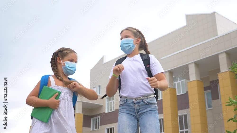 Schoolgirls greet each other with their elbows. Safe elbow greeting in a new reality. Prevention of the spread of Covid19 infection. Children in a protective medical mask. Schoolgirls greet each other with their elbows. Safe elbow greeting in a new reality. Prevention of the spread of Covid19 infection. Children in a protective medical mask.
