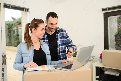 Young couple choosing wall paint color on internet laptop computer for their new house decoration
