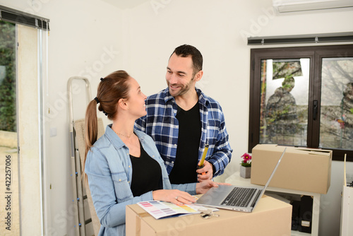 Young couple choosing wall paint color on internet laptop computer for their new house decoration