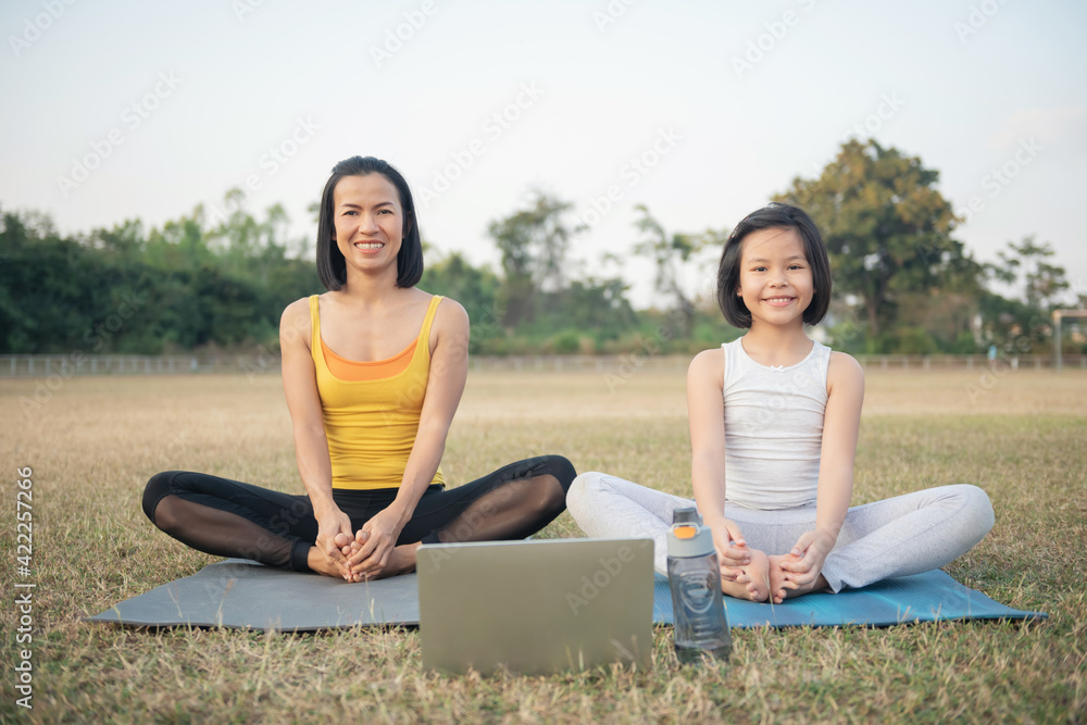 Mother and daughter doing yoga. woman and child training in the park. outdoor sports. healthy sport lifestyle,watching yoga exercises online video tutorial and trying do seated bound angle yoga pose.