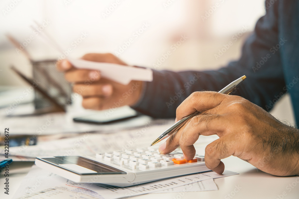 Fototapeta premium Young man was using a calculator to calculate his income and expenses. In his hand there were bills to pay a lot in debt.