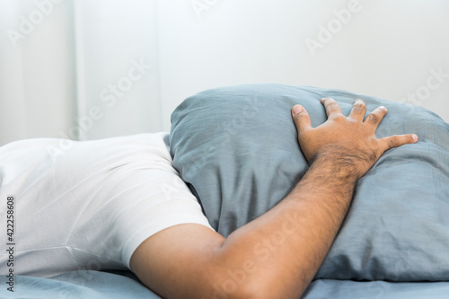 Asian man Lie face down and put a pillow over his head because the side of the house makes a loud noise  disturbing his sleep. He can t sleep until morning.