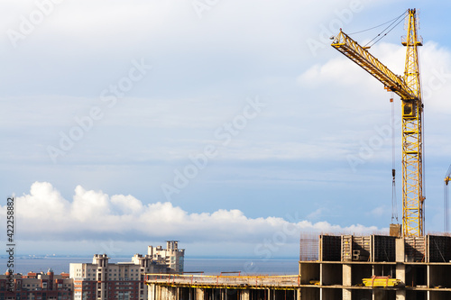 Construction of a high-rise building with a crane. The construction crane and the building against the blue sky background. Business and real estate concept. Photo with copy space