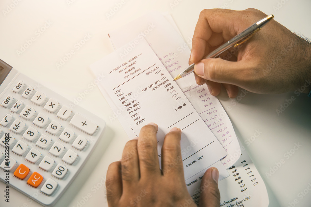 Young man was using a calculator to calculate his income and expenses. In his hand there were bills to pay a lot in debt.