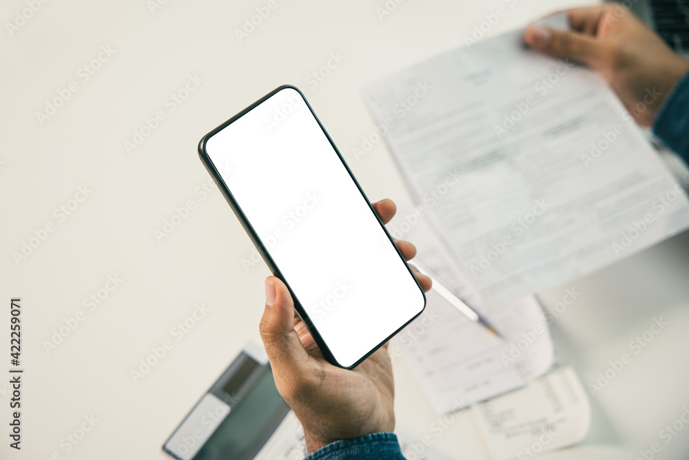 A young man is using a smartphone to scan the bill to calculate his income and expenses. In his hand there were bills to pay a lot in debt.