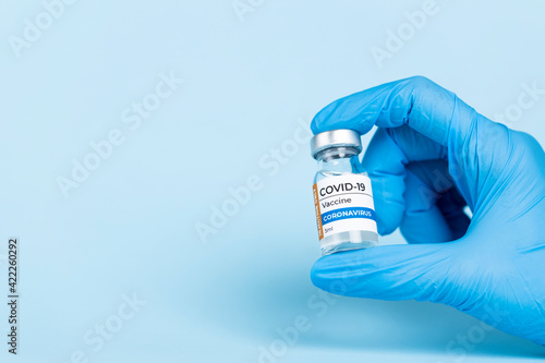Hand in protective glove holds Covid-19 Vaccine glass vial.