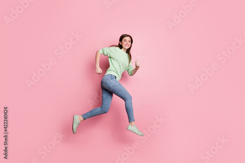 Full size profile photo of brunette nice girl jump run wear lime sweater jeans sneakers isolated on pink color background