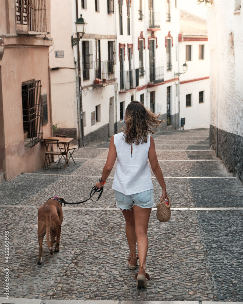 Young woman walking with her dog in the streets of Granada, Spain. Young woman walking with her dog in the streets of Granada, Spain. Concept of friendship between animals and humans Young woman walking with her dog in the streets of Granada, Spain. Young woman walking with her dog in the streets of Granada, Spain. Concept of friendship between animals and humans